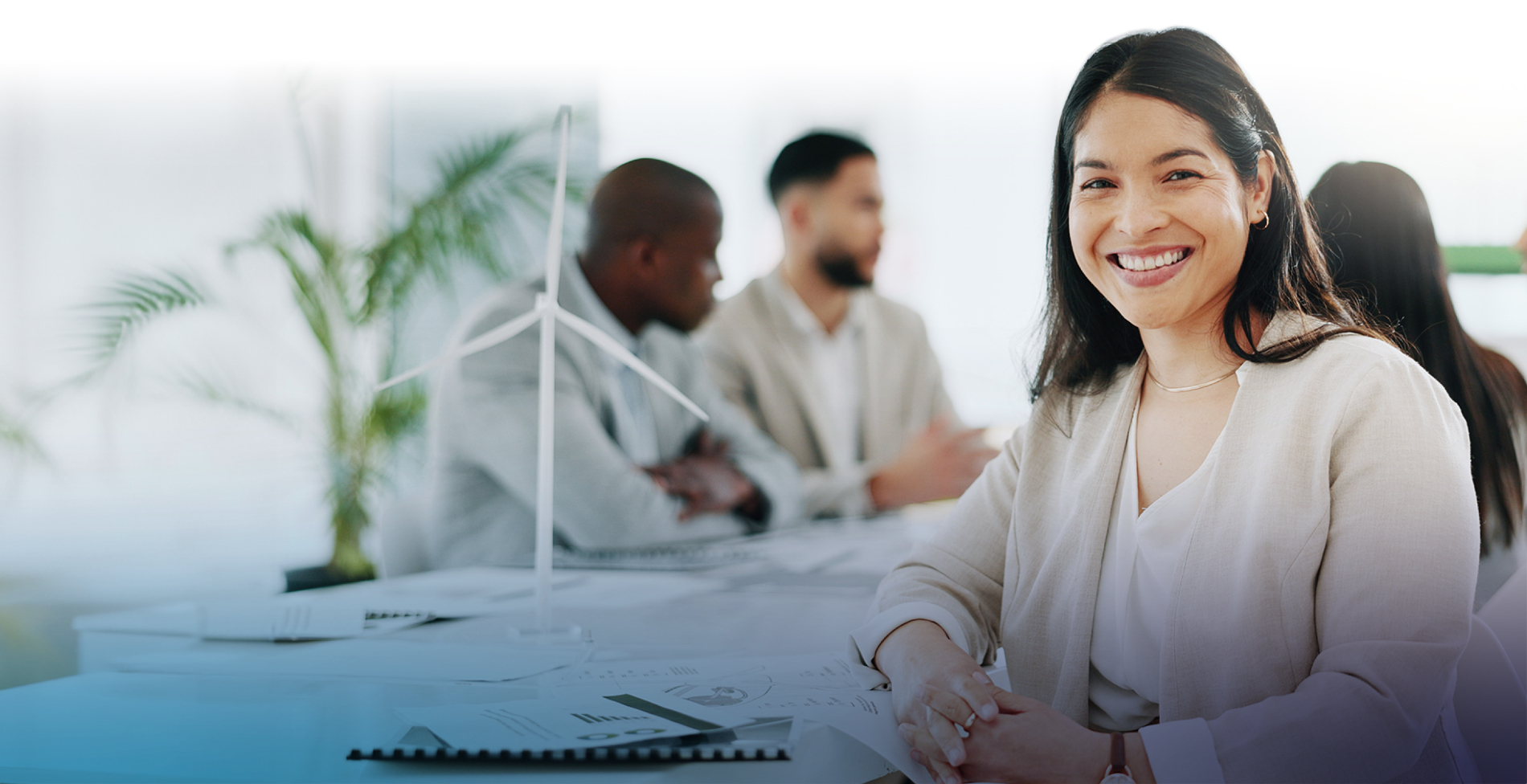 Woman smiling while sitting at a desk while two coworkers are chatting in the background.