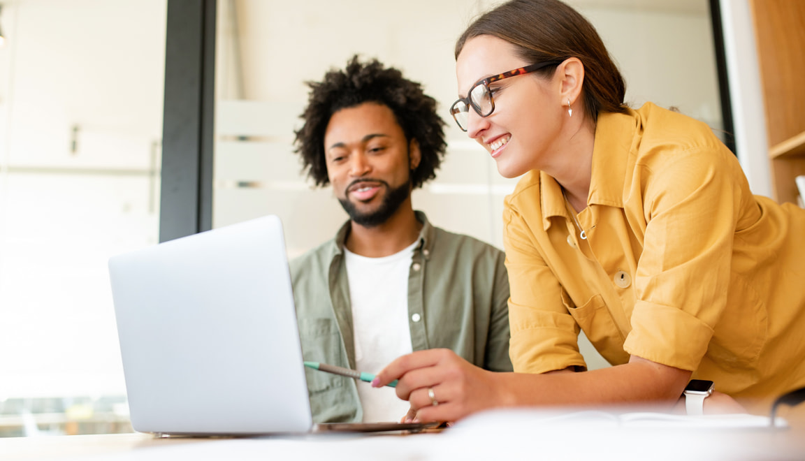 Two smiling coworkers reviewing something on a laptop together.