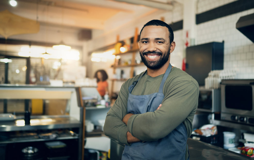 Confident frontline manager smiling with arms crossed, standing in a coffee shop setting.