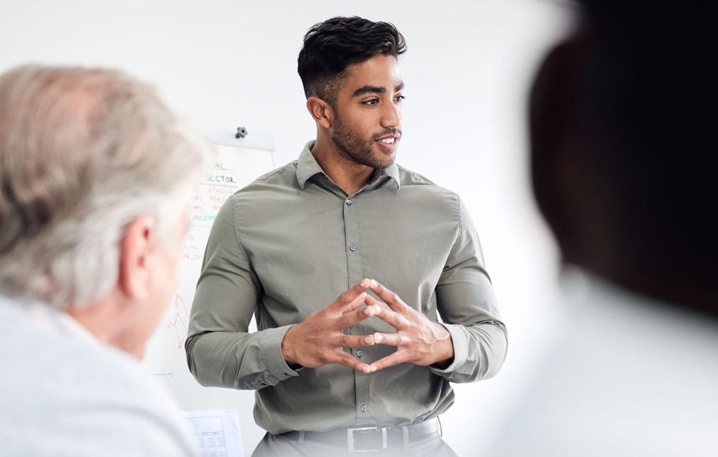 Man standing with his hands clasped together while presenting to a group.