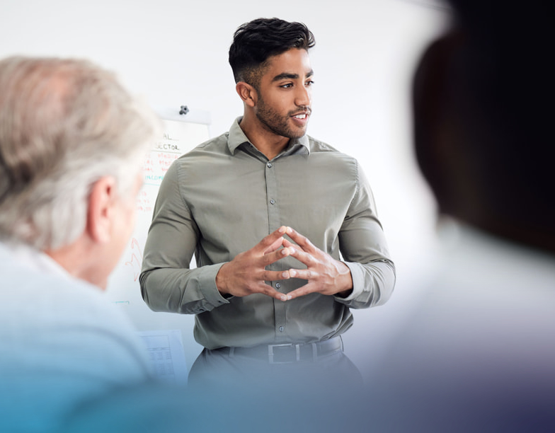 Man standing with his hands clasped together while presenting to a group.