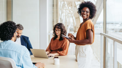 Woman standing while a group of coworkers work at their laptops.