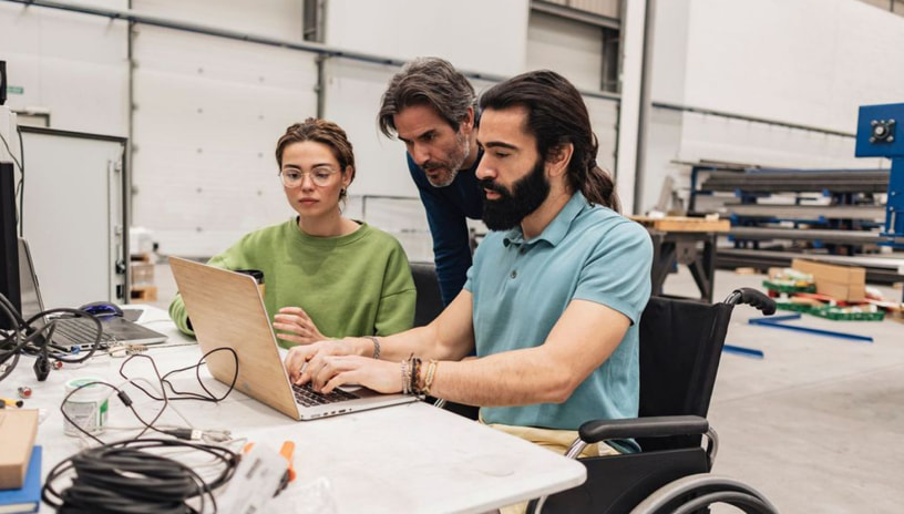 Three coworkers reviewing something on a laptop in a warehouse setting.